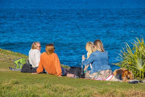 a group of women sitting on the grass near the water at Hastings Cove Holiday Apartments in Hastings Point