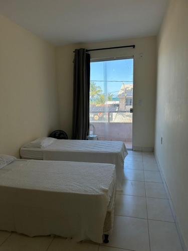 two beds in a room with a large window at Residencial Edite Bulhões in Guaibim