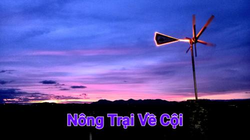 a wind turbine in front of a sunset at Nông Trại Về Cội - The Original Farm in Buôn Bedeur