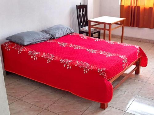 a red bed with a red blanket with a table at Hospedaje Arana in Chincha Alta