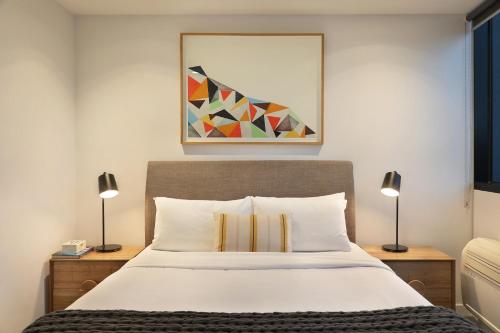 a bedroom with a bed with two lamps and a painting at The Canvas Apartment Hotel in Melbourne