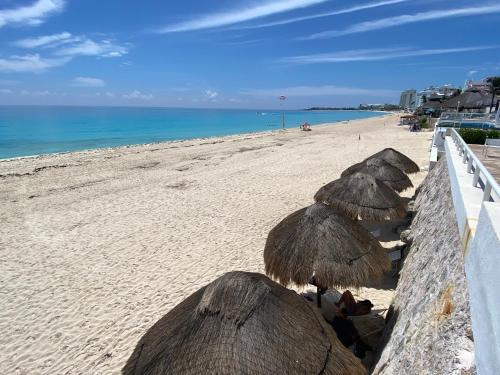 a group of straw umbrellas on a beach at Brisas Shores Penthouse Beachfront, Ocean View Terrace Cancun Hotel Zone, 2 bedrooms in Cancún