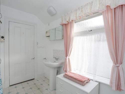 un baño con lavabo y una ventana con cortinas rosas. en Bro Dawel, en Beaumaris