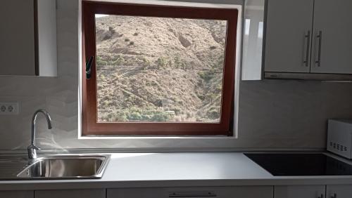 a window over a sink in a kitchen with a mountain at CASA DEL ARBOL DE BIBIANA 2 in Hermigua