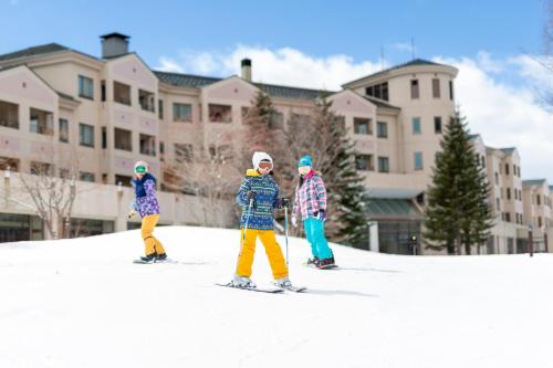 北塩原村的住宿－EN RESORT Grandeco Hotel，三个孩子在雪中滑雪,在建筑物前