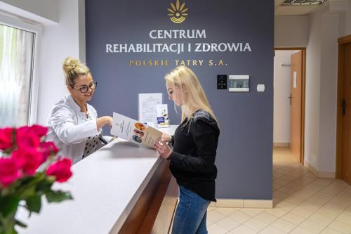 Eine Frau überreicht einer anderen Frau an einem Tresen eine Schachtel. in der Unterkunft Zespół Dolina Białego - Pensjonat Telimena in Zakopane