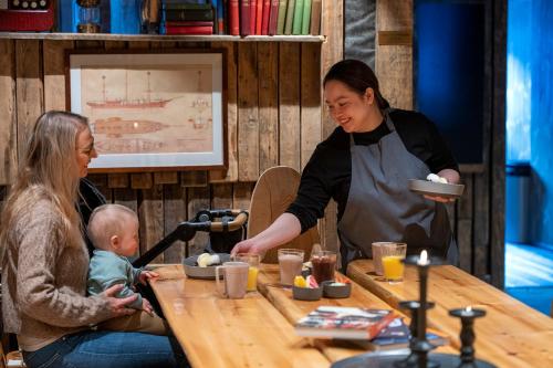 a woman holding a plate and a woman holding a baby at a table at Basecamp Hotel in Longyearbyen