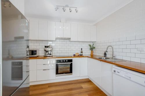a white kitchen with white appliances and wooden floors at Bermagui Townhouse - Amazing views & location in Bermagui