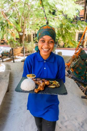 a woman holding a plate of food on a tray at Makofi Guest House in Nungwi