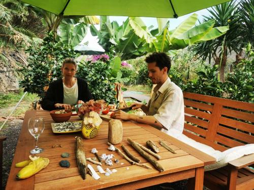 Dos personas sentadas en una mesa de madera con comida. en Eco Finca in Paradise Valley Azuaje, en Firgas
