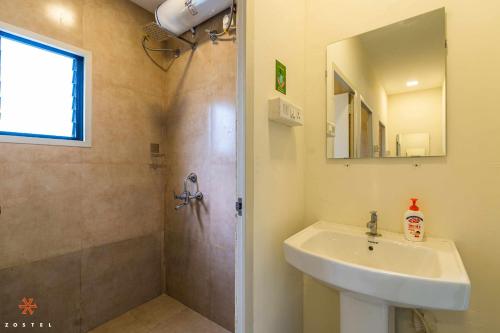uma casa de banho com um lavatório e um chuveiro com um espelho. em Zostel Pune (Viman Nagar) em Pune