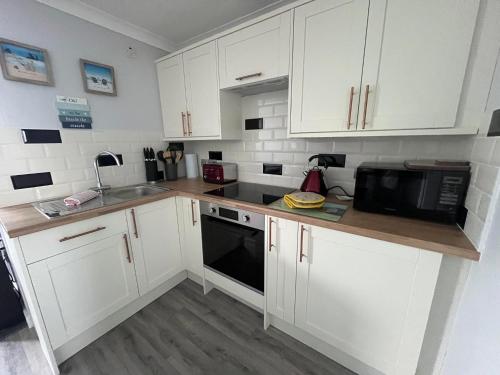 a kitchen with white cabinets and a black microwave at 246, Two bed Chalet on Belle Aire Holiday Park - sleeps 5, pet friendly, free Wi-Fi, bed linen and towels included plus onsite entertainment available in Great Yarmouth