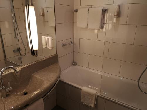 een badkamer met een bad, een wastafel en een spiegel bij Mercure Bonn Hardtberg in Bonn