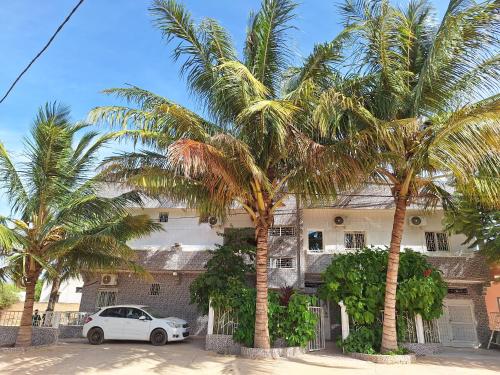 a white car parked in front of a building with palm trees at La Mboroise in Mboro