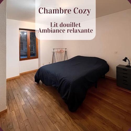 um quarto com uma cama com um cobertor preto num piso de madeira em Appartement 1er étage calme parking gratuit à 1 min à pieds em Roanne