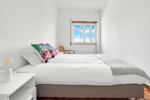 a white bedroom with a bed and a window at Sunny Apt in Almada with Tejo View in Almada