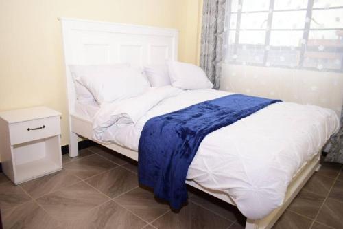 a bedroom with a white bed with a blue blanket on it at Crystal Homes Nanyuki Haven 2-BR Gem in Nanyuki