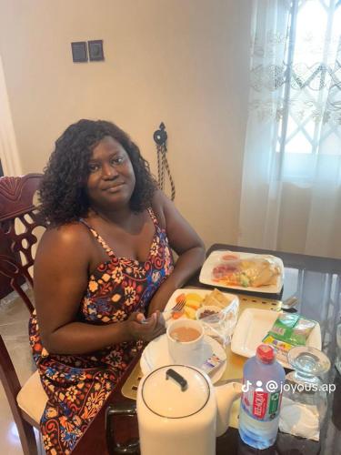 a woman sitting at a table with a plate of food at Joyous AP Guest House in Aburi