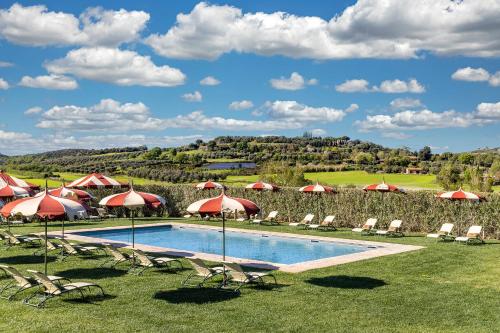 a swimming pool with umbrellas and chairs and a field at Locanda Rossa in Capalbio