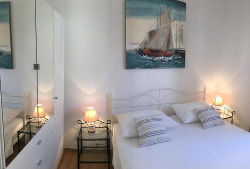 a bedroom with a white bed with a sailboat painting on the wall at Apartments Eastern Paradise in Bol