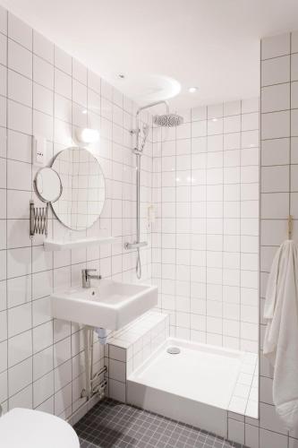 La salle de bains est pourvue de carrelage blanc, d'un lavabo et d'une baignoire. dans l'établissement Hotel Beaulieu Lyon Charbonnières, à Charbonnières-les-Bains