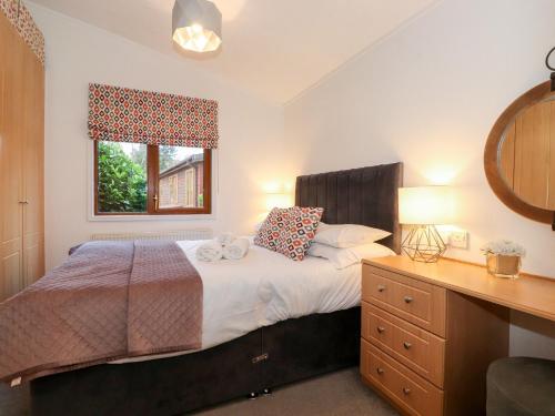 a bedroom with a bed with a dresser and a window at Ruskin Lodge in Windermere