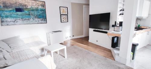 a white living room with a white couch and a tv at Luxueux appartement sur jardin in Paris