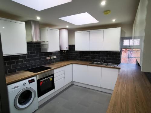 a kitchen with white cabinets and a washer and dryer at The Old Guest House, Norbury Avenue in Norbury