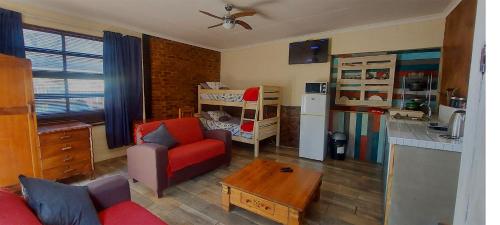 a living room with a red couch and a kitchen at THE POT AIRBNB, FAERIE GLEN, PRETORIA EAST in Pretoria