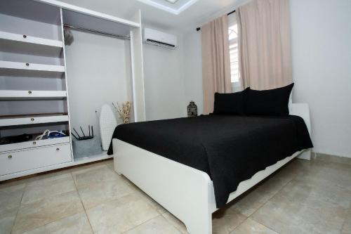 a white bedroom with a black bed and a window at EcoMar Rentals Casa:, Naturaleza, Piscina & Playa in Cabo Rojo