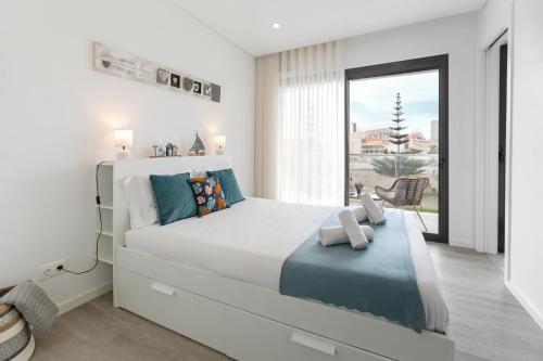 a white bedroom with a large bed and a window at Consolação Wave Beach House in Atouguia da Baleia