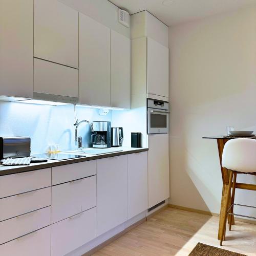a kitchen with white cabinets and a table and a stool at Pramea Apartments Pikku Pietari in Kuopio