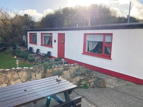 ein weißes Haus mit roten Fenstern und einer Holzbank in der Unterkunft The Potters Cottage in Clifden