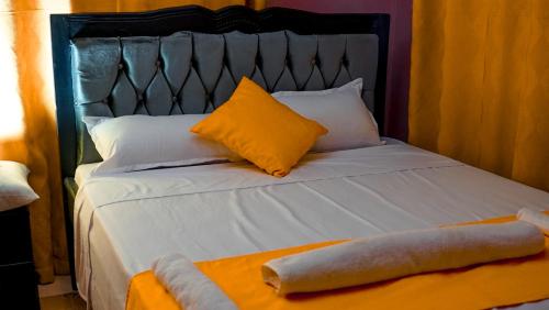 uma cama branca com uma cabeceira preta e almofadas amarelas em Kate's 1 bedroom furnished apartment em Kisumu