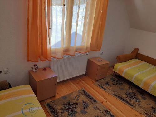 1 dormitorio con 2 camas y una ventana con cortinas de color naranja en Vikend kuća Vukašinović, en Kopaonik