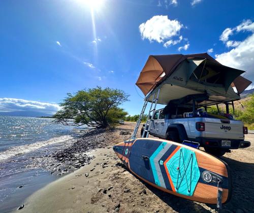 um camião estacionado numa praia com um barco em Embark on a journey through Maui with Aloha Glamp's jeep and rooftop tent allows you to discover diverse campgrounds, unveiling the island's beauty from unique perspectives each day em Paia