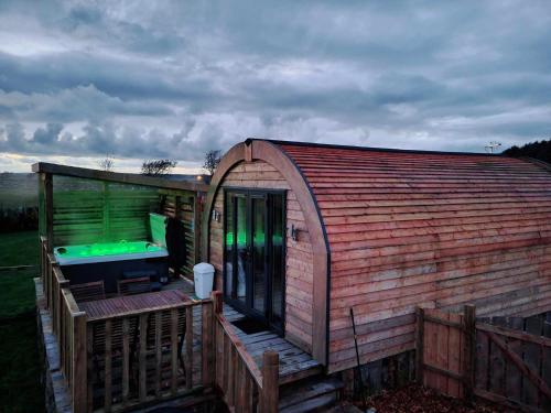 a large wooden building with a deck with a green light at Beautiful Glamping Pod with Central Heating, Hot Tub, Garden, Balcony & views - close to Cairnryan - The Herons Nest by GBG in Glenluce