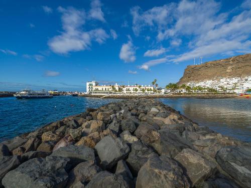 a group of rocks in the water with buildings in the background at Sunny Valley Apartment in Mogán