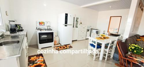 a kitchen with white appliances and a table and chairs at Camelo locação de Suítes Individuais Pousada com Cozinha e Sala Compartilhada in Arroio do Silva