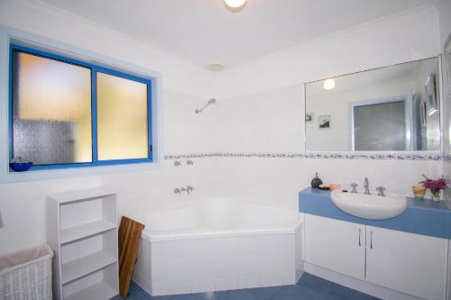 a white bathroom with a tub and a sink at Banksia Waters in Lakes Entrance
