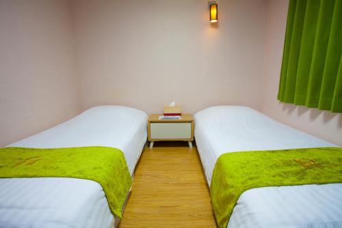 two beds in a small room with green sheets at Jeju R Hotel & Guesthouse in Jeju