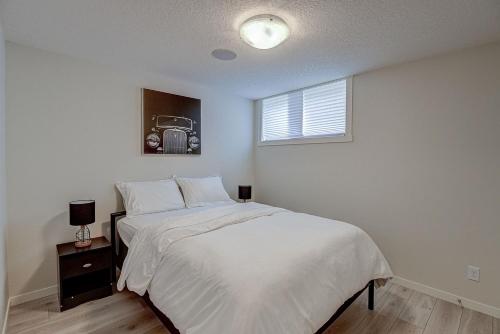 a bedroom with a bed with white sheets and a window at Cozy New Suite in Seton, South Calgary in Calgary