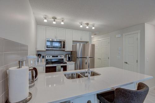 a white kitchen with a sink and a refrigerator at Cozy New Suite in Seton, South Calgary in Calgary