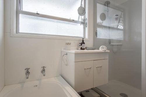 a white bathroom with a tub and a sink and a window at Sea Breeze On Belt By Coastal Walkway in New Plymouth