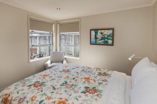 a bedroom with a bed with a floral bedspread and a chair at City Sails Central Location in New Plymouth