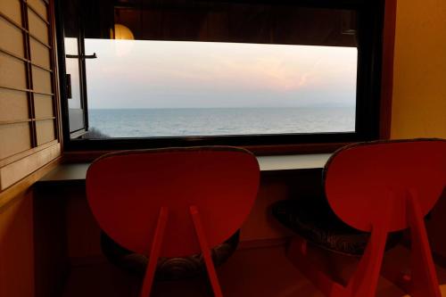 two red chairs looking out a window at the ocean at 海のほてる　いさば in Numazu