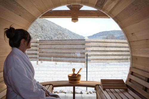 a woman sitting at a table looking out of a window at Chalet Authentique - Insolite - Sauna & Télécabine - Ménage, serviettes, lit fait inclus in Rochesson