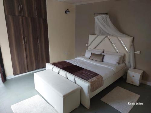 a bedroom with a large white bed and a stool at Boffar Cabin 6 in Naivasha