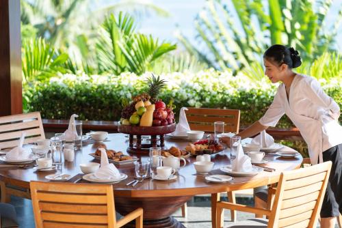 a woman standing at a table with a bowl of fruit at Andara Resort Villas in Kamala Beach