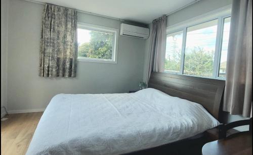 a bedroom with a white bed and two windows at 8 mins drive to the airport in Christchurch